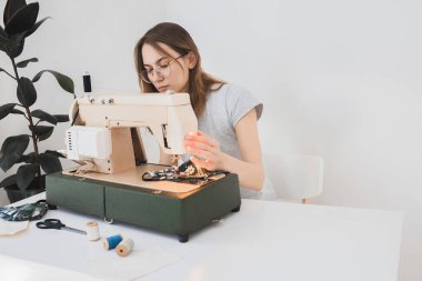 Gribi önlemek için evdeki dikiş makinesine koruyucu ilaç maskesi takan bir kız. Covid-19 beyaz arka plan ev işyeri olan odada.