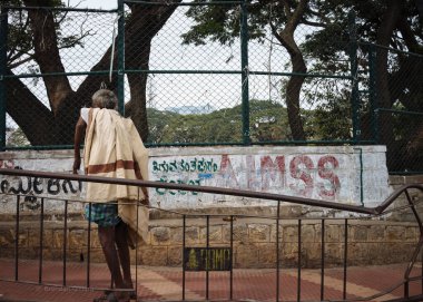 Kolunda deformasyon olan bir adam Bangaluru, Karnataka, Hindistan 'da kaldırımda eğilmiş duruyor.
