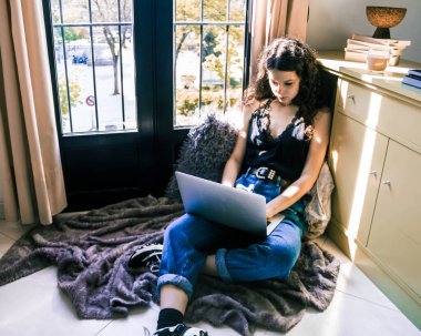 Pencerenin yanında dizüstü bilgisayarla çalışan genç bir kız.