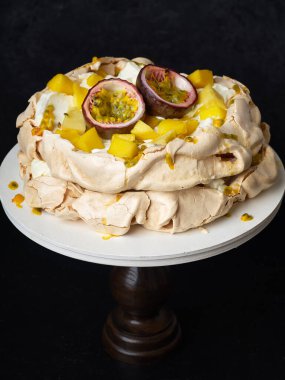 Tutku meyveli Pavlova keki, mango, limon ve muz kreması koyu arkaplanda.