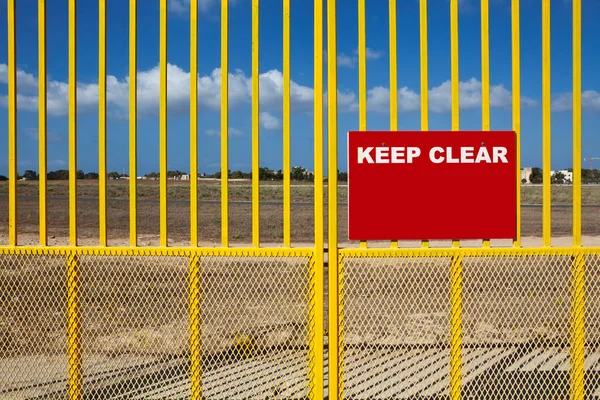 A red Keep Clear warning sign with copyspace on a bright yellow metal barrier or gate