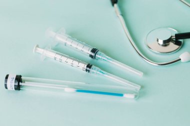 Steteskopun yanında iki steril şırınga ve test tüpünde bir çubuk.