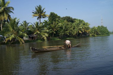 Ağzında sigara olan bir adam, uzun ve dar bir kanoda durur ve Kerala 'nın durgun sularından bir balıkçı ağı çeker, palmiye ağaçları arka planda dik durur..