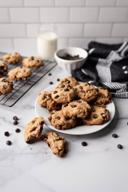 Beyaz mermer tezgahta çikolatalı kurabiye ve süt tabağı..