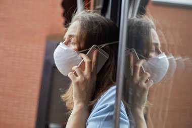 Cep telefonu kullanan maskeli bir kadın Covid-19 zamanlarındaki endişelerini gösteriyor.