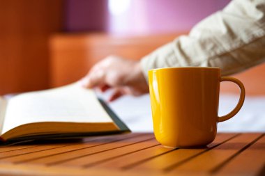 Sarı kahve ve kitabın sayfasını çeviren bir adam. Okuma konsepti.