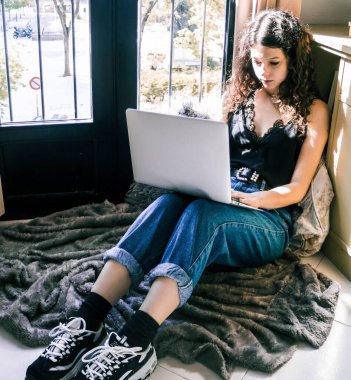 Pencerenin yanında dizüstü bilgisayarla çalışan genç bir kız.