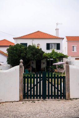 Çatı kiremitli beyaz villa ve önünde yeşil ahşap kapı..