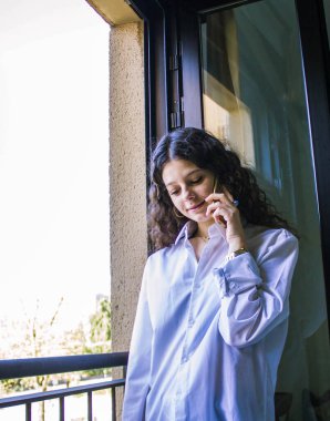 Genç kız pencerede telefonla konuşuyor.