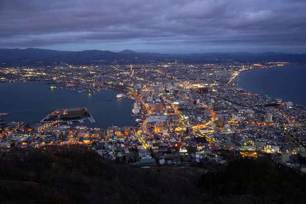 Hakodate, Japonya - 30 Kasım 2019: Hakodate Dağı 'ndan Milyon Dolarlık Manzara, etekten zirveye giden yolu takip edin. Parıldayan şehir ışıklarının ve okyanusun zifiri karanlığının karşıtlığı tarif edilemez derecede güzeldir..