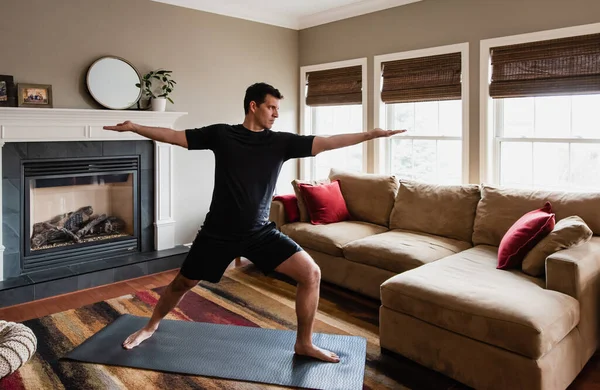 Fit man doing warrior yoga pose at home in his living room.