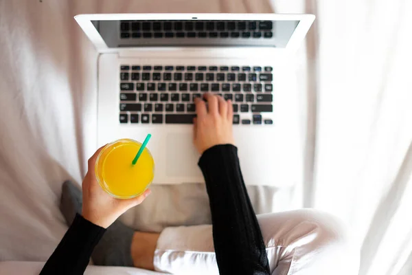 Hand picking up an orange juice next to a laptop. Juice and work concept.