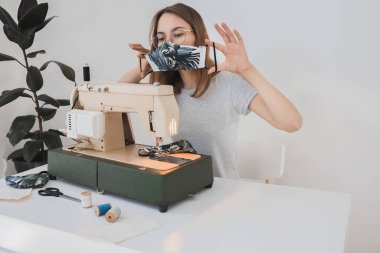 Gribi önlemek için evdeki dikiş makinesine koruyucu ilaç maskesi takan bir kız. Covid-19 beyaz arka plan ev işyeri olan odada.
