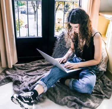 Pencerenin yanında dizüstü bilgisayarla çalışan genç bir kız.