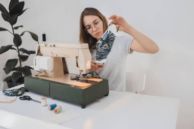 Gribi önlemek için evdeki dikiş makinesine koruyucu ilaç maskesi takan bir kız. Covid-19 beyaz arka plan ev işyeri olan odada.