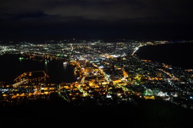 Hakodate, Japonya - 30 Kasım 2019: Hakodate Dağı 'ndan Milyon Dolarlık Manzara, etekten zirveye giden yolu takip edin. Parıldayan şehir ışıklarının ve okyanusun zifiri karanlığının karşıtlığı tarif edilemez derecede güzeldir..
