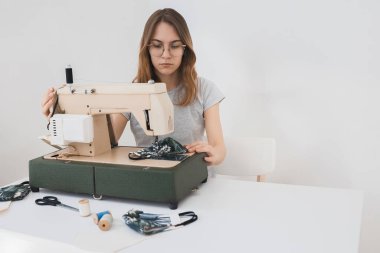 Gribi önlemek için evdeki dikiş makinesine koruyucu ilaç maskesi takan bir kız. Covid-19 beyaz arka plan ev işyeri olan odada.