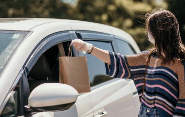 Eldivenli ve yüz maskeli bir kadın arabanın yanında kese kağıdı taşıyor. Covid19 salgını sırasında teslimat hizmetleri kavramı.