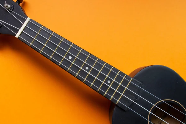 Body of a bright black ukulele guitar against a bright orange background (minimalism style), copy space for text