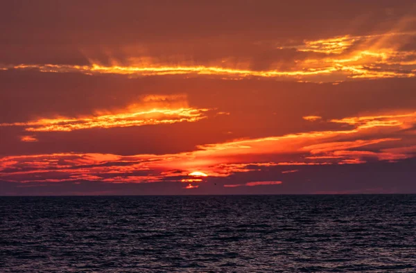 Sun setting at ocean horizon as sky catches fire.