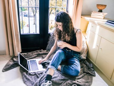 Pencerenin yanında dizüstü bilgisayarla çalışan genç bir kız.