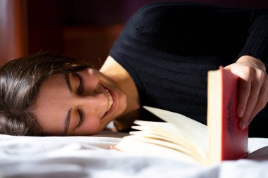 Kadın yatakta uzanıyor ve kitap okuyor..