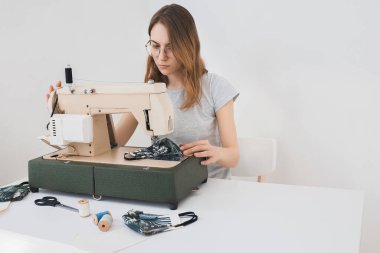 Gribi önlemek için evdeki dikiş makinesine koruyucu ilaç maskesi takan bir kız. Covid-19 beyaz arka plan ev işyeri olan odada.