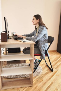Ceketli genç bir kadın evde bilgisayar başında çalışıyor.