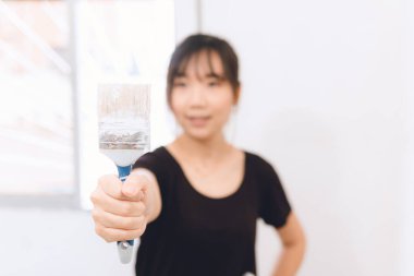 Duvarı boyamak için boya fırçası kullanan Asyalı kadın.