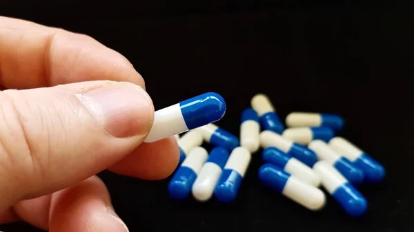 Blue and white pharmacy capsules on black background