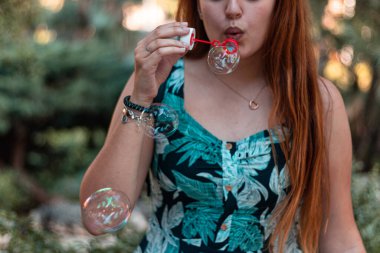 Parkta ya da doğal ortamda sabun köpüğüyle oynayan genç bir kız