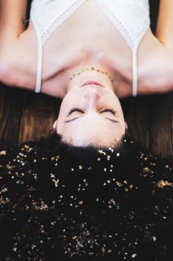 Genç bir kadın portresi. Saçında bir sürü çiçekle tahtada yatıyor.