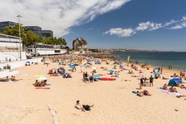 Portekiz, Lizbon yakınlarındaki Cascais 'de güneşli bir yaz haftasonu geçiren yerliler ve turistlerle dolu bir plaj.