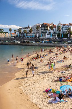 Portekiz, Lizbon yakınlarındaki Cascais 'de güneşli bir yaz haftasonu geçiren yerliler ve turistlerle dolu bir plaj.