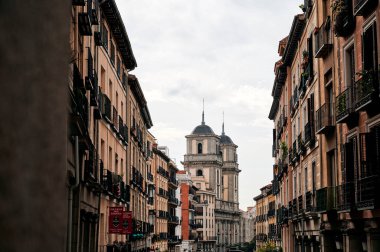 Madrid 'in geleneksel mimarisi. Dar sokaktaki renkli binalar ve bulutlu gökyüzüne karşı katedral.