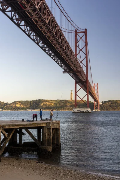 ポルトガル リスボン中心部のTejo川にある25 Abil Bridgeの下で釣りをする人々への美しい眺め — ストック写真