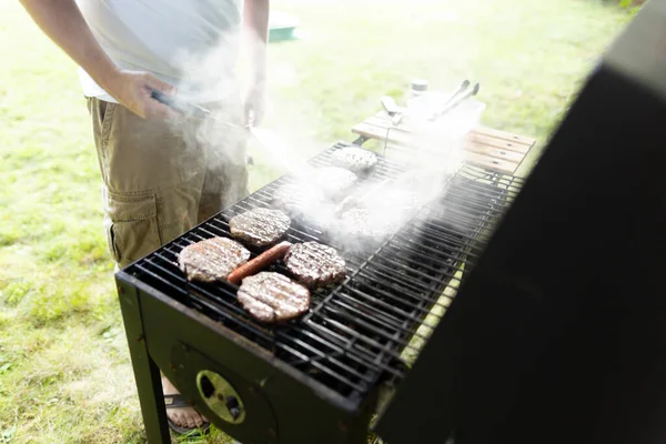 男人站在烟雾弥漫的后院烤架上翻炒汉堡包和热狗 — 图库照片