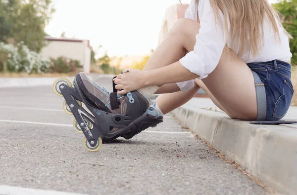 Blonde girl in a white blouse, jeans and skates tying her laces. Roller-skating concept