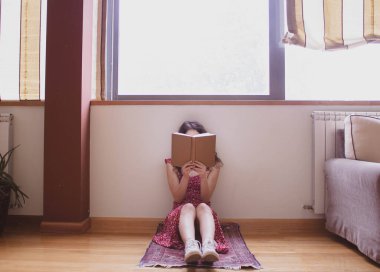 Gündüz kitap okuyan genç bir kız pencerenin yanında.