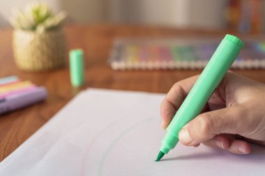 Evde renkli kalemlerle çizen bir kadının elleri.