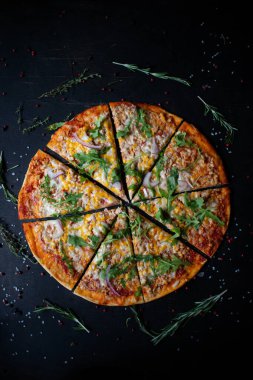 Geleneksel İtalyan pizzası. Dilimler halinde dilimlenmiş lezzetli taze pizza otlar ve peynirle koyu bir arka planda. Üst Manzara. Pizza siyah masada. Seçici odak.