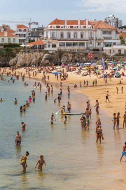 Portekiz, Lizbon yakınlarındaki Cascais 'de güneşli bir yaz haftasonu geçiren yerliler ve turistlerle dolu bir plaj.