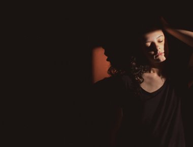 Siyah arka planda genç bir kadın, yüzünde ışık ve gölgeler var.