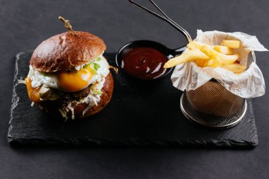 Köfteli hamburger ve yumurta, patates kızartması ve siyah arka planda sos.