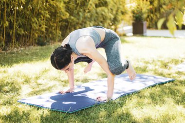 Bahçede minderle yoga yapan genç bir kız.