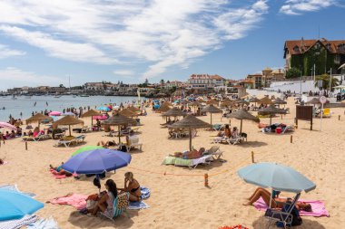 Portekiz, Lizbon yakınlarındaki Cascais 'de güneşli bir yaz haftasonu geçiren yerliler ve turistlerle dolu bir plaj.