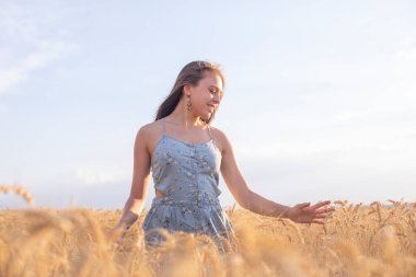 Gün batımında buğday tarlasında yürüyüş yapan genç bir kadın.