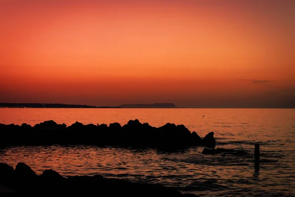 日没後のスカイライン 岩のシルエットと海の波とオレンジの空の風景 海岸線の写真でオレンジの夕日 休暇中の楽園のウォーターフロント静けさ 雄大な水平線の壁紙 — ストック写真