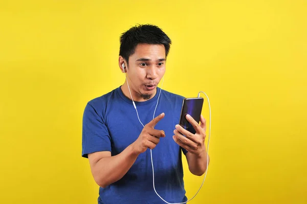 兴奋的亚洲男人的画像惊讶地发现网上有一首流行的歌曲 在黄色背景下被隔离开来 — 图库照片