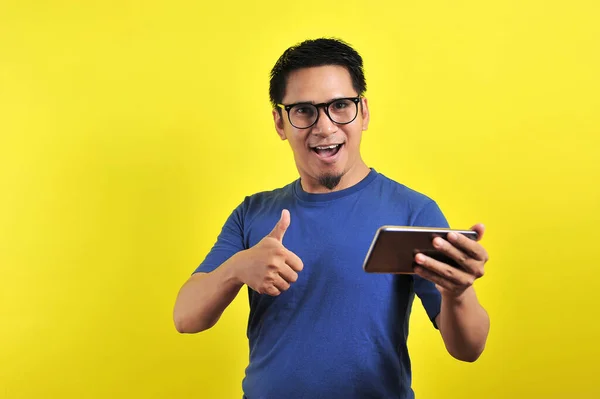 很高兴年轻英俊的亚洲男人用黄色背景的智能手机微笑 — 图库照片
